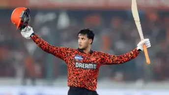 Abhishek Sharma of Sunrisers Hyderabad celebrates scoring 141 runs in IPL 2025, holding his bat high in a floodlit stadium with fireworks in the sky and a cheering crowd in the background.