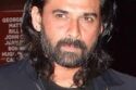 Portrait of Indian actor Mukul Dev smiling, wearing a formal suit, in a dimly lit background.