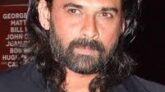 Portrait of Indian actor Mukul Dev smiling, wearing a formal suit, in a dimly lit background.