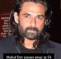 Portrait of Indian actor Mukul Dev smiling, wearing a formal suit, in a dimly lit background.