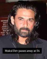 Portrait of Indian actor Mukul Dev smiling, wearing a formal suit, in a dimly lit background.