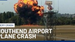 Wreckage of small medical plane crash in flames at London Southend Airport with smoke billowing into the sky, emergency responders on scene.