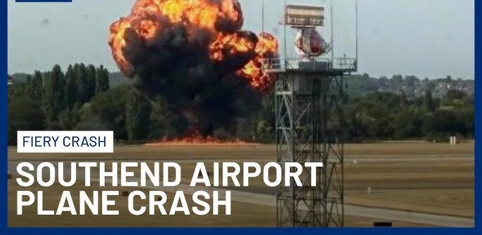 Wreckage of small medical plane crash in flames at London Southend Airport with smoke billowing into the sky, emergency responders on scene.